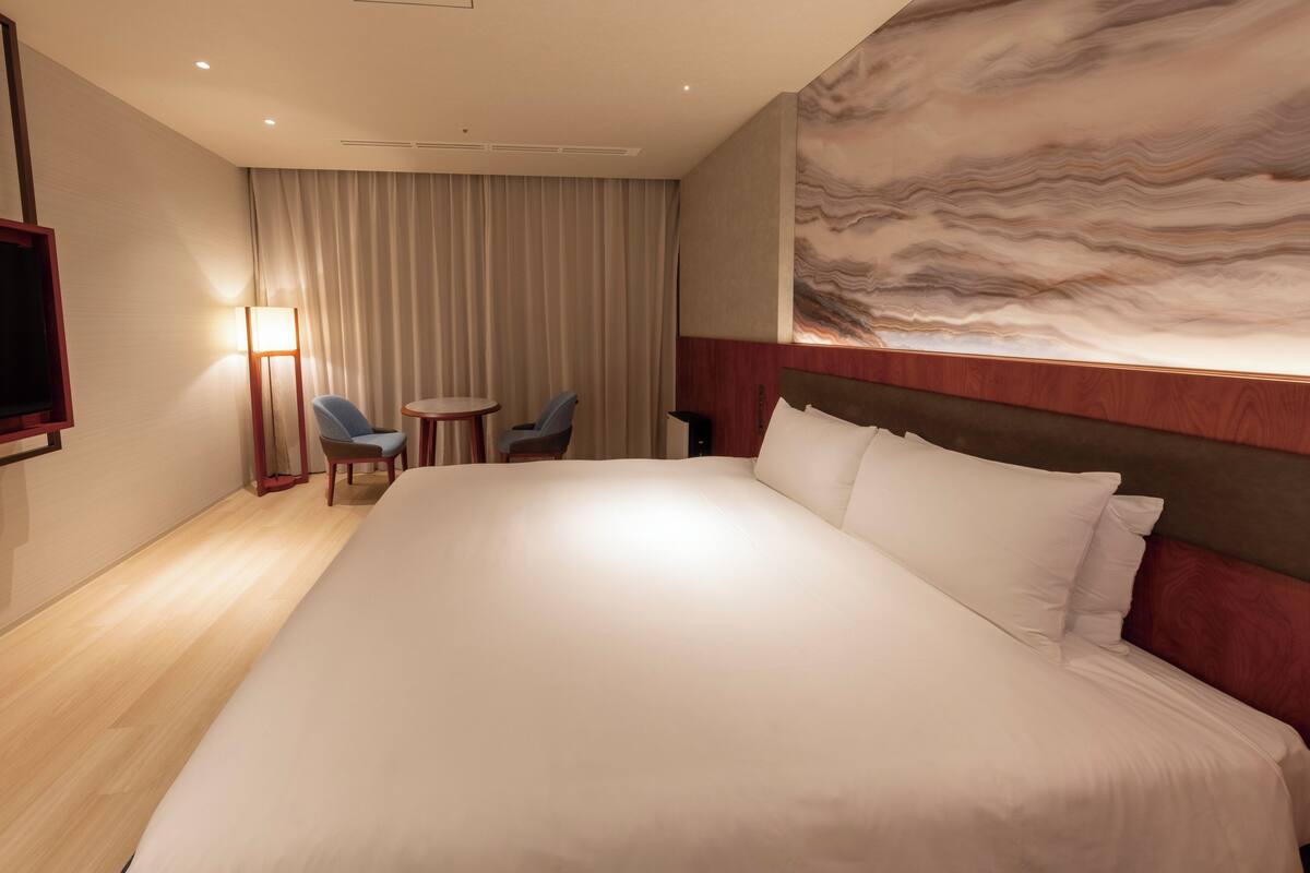 Ein Hotelzimmer mit einem großen Bett, einem Flachbildfernseher, einem Schreibtisch mit zwei Stühlen und einem großflächigen Wandbild.