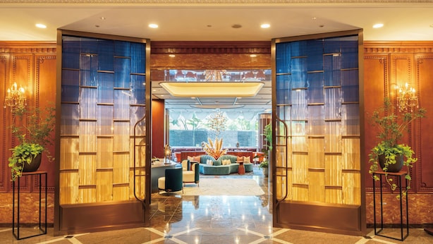 Um hall de hotel com entrada imponente, área de estar com sofás e mesa de centro, e uma grande janela com vista para o exterior.