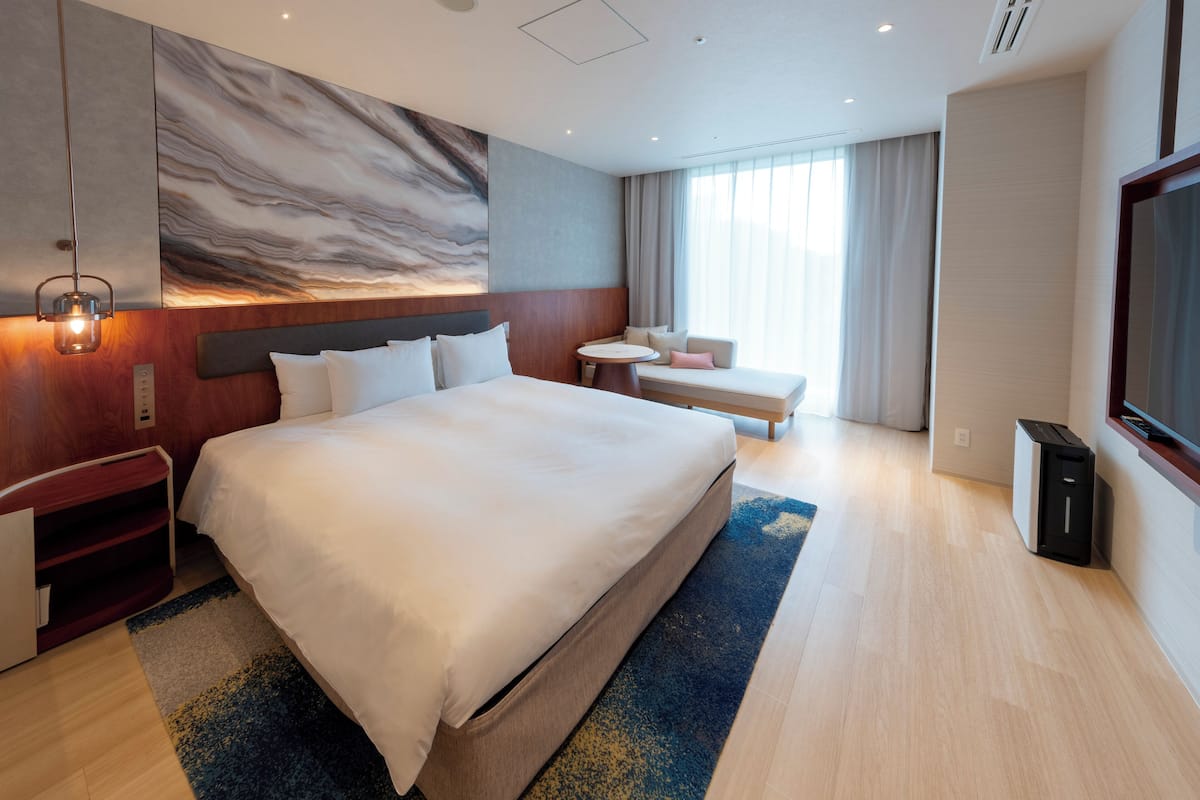 Ein modernes Hotelzimmer mit einem großen Bett, einer kleinen Sitzecke, einem Fernseher und einer Marmorwand.