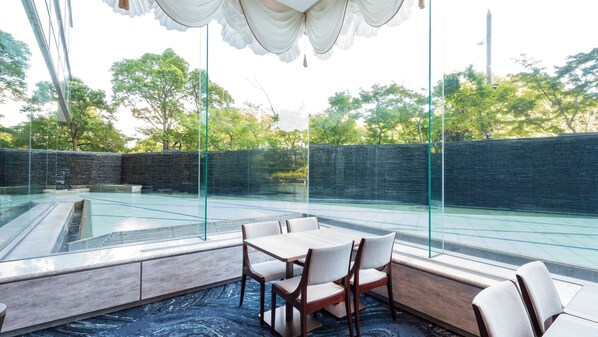Un espace extérieur moderne, aménagé avec des murs en verre, une piscine et offrant une vue sur les arbres et un mur de pierre.