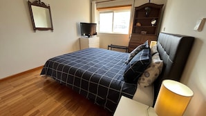 A bedroom with a bed, a television, a dresser, and a window. - Vila do Conde Beach Apartment  (Vila do Conde)