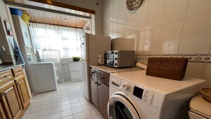 A compact kitchen with a washing machine, a microwave, and a small refrigerator. - Vila do Conde Beach Apartment  (Vila do Conde)