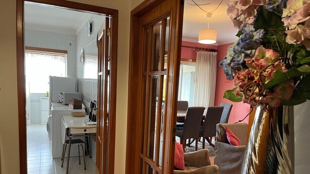 A kitchen with a dining area, a vase with flowers, and a view of the dining room. - Vila do Conde Beach Apartment  (Vila do Conde)