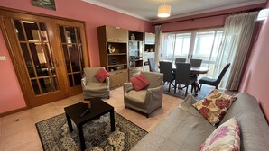 A living room with a sofa, two armchairs, a coffee table, and a dining area with chairs and a table. - Vila do Conde Beach Apartment  (Vila do Conde)