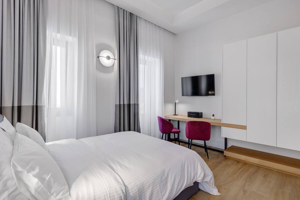 Habitación de hotel moderna con una cama grande, un escritorio con silla, un televisor de pantalla plana y una pequeña planta.