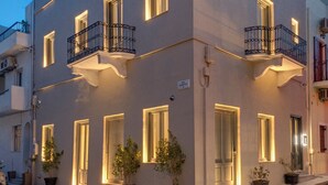 A modern two-story building with balconies, potted plants, and a cobblestone street. - Times Elegant Rooms (Syros)