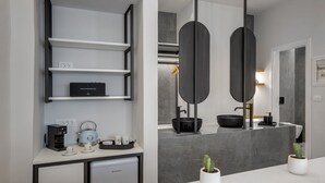 A modern bathroom with a grey marble countertop, a black sink, and a large mirror. There are two white potted plants on the counter. - Times Elegant Rooms (Syros)