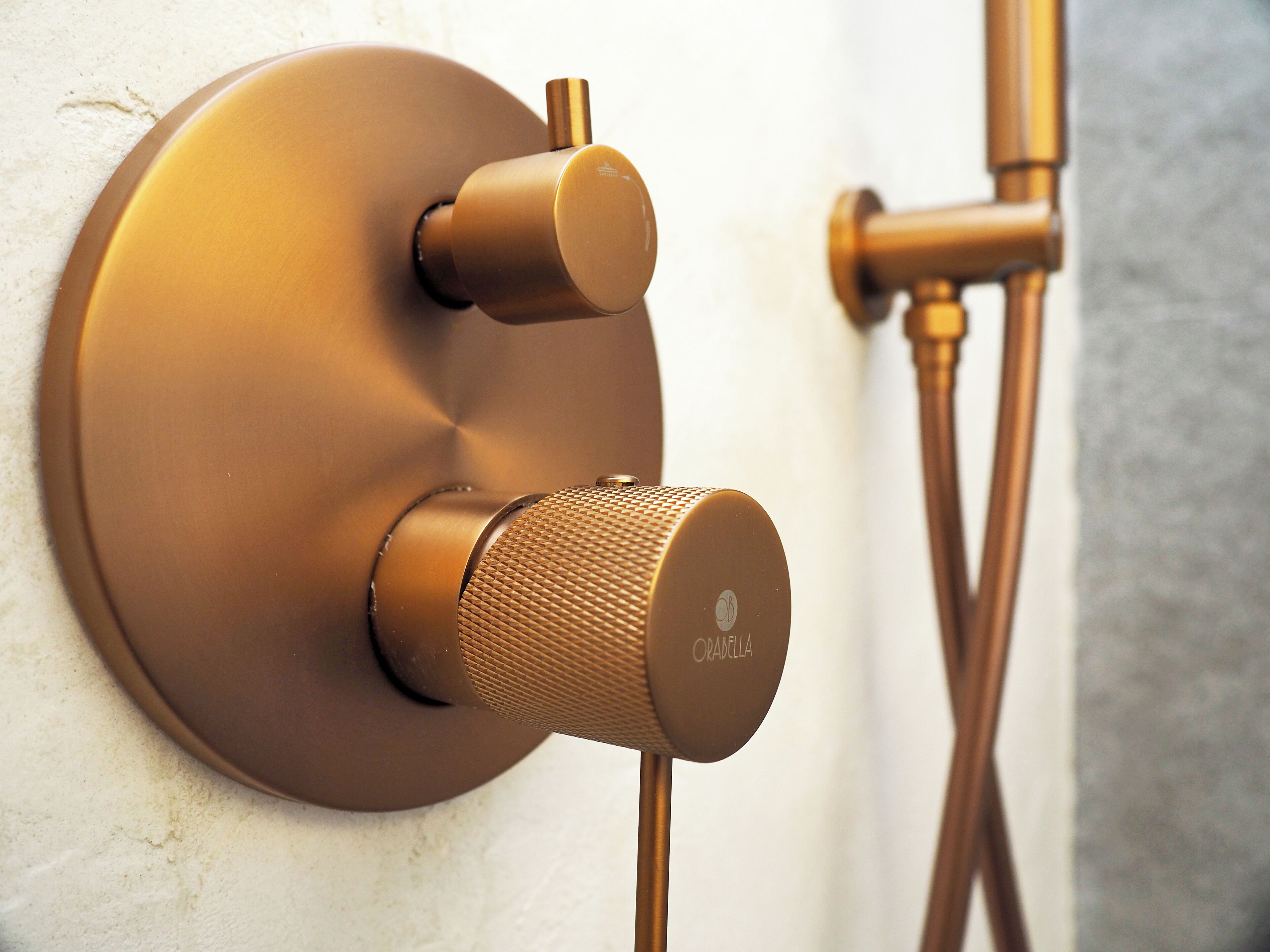 A wall-mounted shower control with a round, metallic finish and a textured knob.