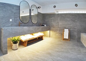 A modern bathroom with a large mirror, a wooden bench, and a towel rack. - Times Elegant Rooms (Syros)