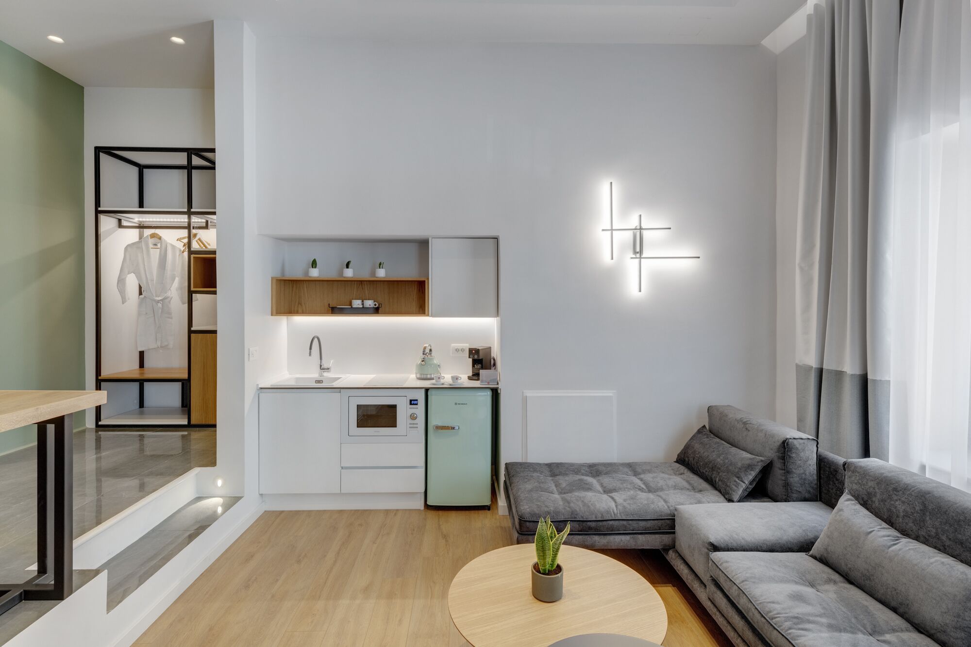 A modern living room with a grey sectional sofa, a round coffee table with a plant, and a kitchen area with a sink and cabinets.