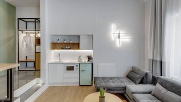 A modern living room with a grey sectional sofa, a round coffee table with a plant, and a kitchen area with a sink and cabinets.