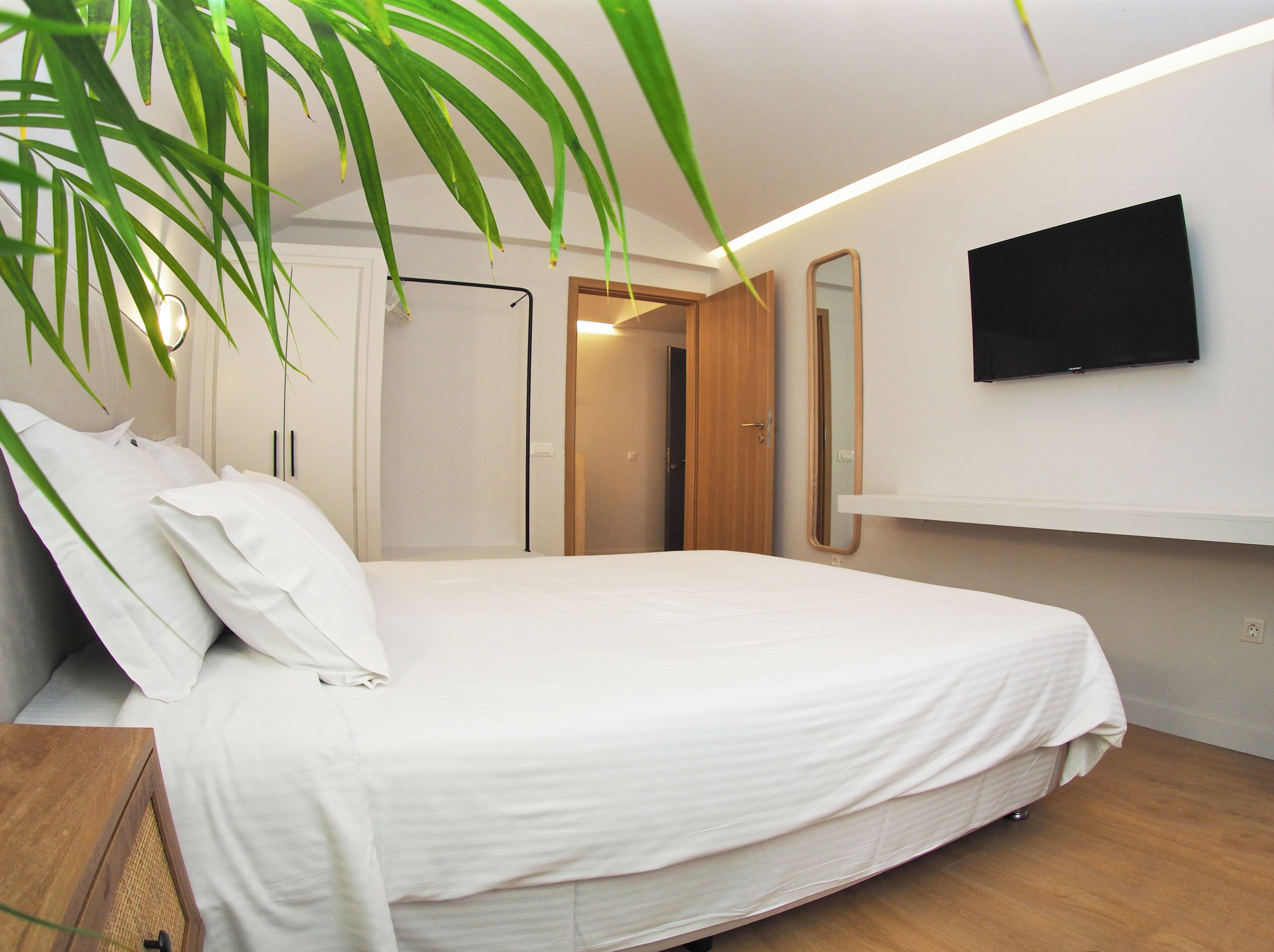 A modern bedroom with a large bed, a TV mounted on the wall, and a wooden door leading to another room.