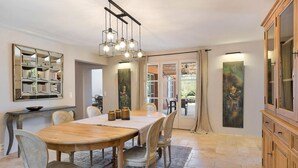 A dining area with a wooden table and chairs, a chandelier, a cabinet, and a painting on the wall.