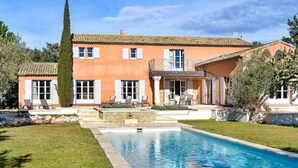 A two-story building with a swimming pool, outdoor seating, and a stone wall.