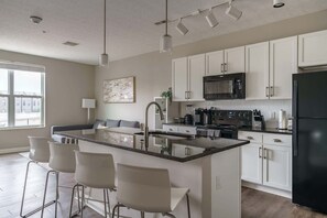 Une cuisine moderne dotée d’un îlot central, de meubles blancs, d’appareils électroménagers en acier inoxydable et de tabourets de bar.