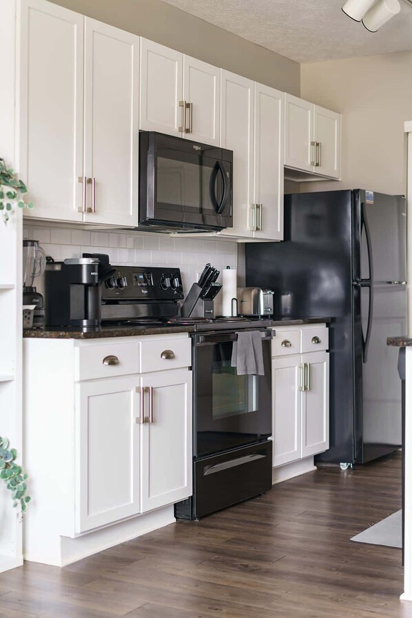 Una cocina moderna con armarios blancos, un refrigerador negro, un microondas, una estufa y una cafetera.