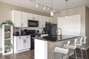 A modern kitchen with white cabinets, a central island with bar stools, a black refrigerator, and a microwave.