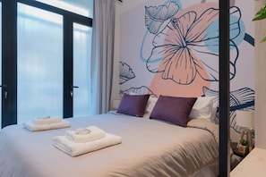 Une chambre d’hôtel avec un lit, des oreillers, un mur décoré d’œuvres d’art florales et une fenêtre avec des rideaux.