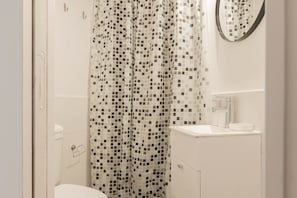 Une salle de bain avec une douche munie d’un rideau carrelé, des toilettes, un lavabo et un miroir.