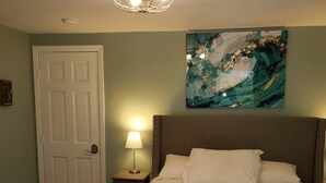 Ein ordentlich bezogenes Bett mit Kopfteil, einer Nachttischlampe und einer Tür links.