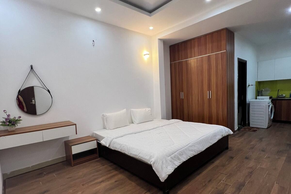 A modern bedroom with a large bed, wooden wardrobe, and a small kitchenette.