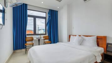 Habitación de hotel con una cama grande, un escritorio con dos sillas, una ventana con cortinas y vistas a edificios.