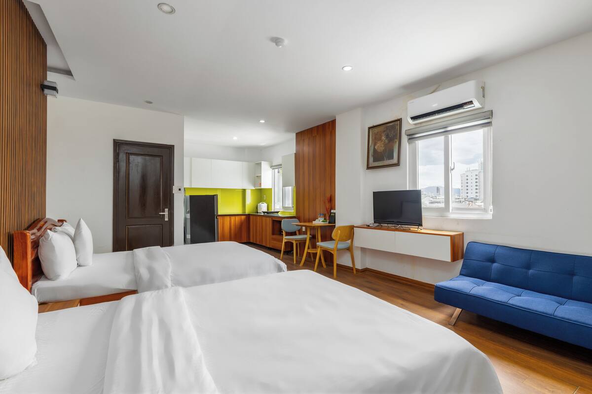 A hotel room with two beds, a desk, a chair, a TV, and a window with a city view.