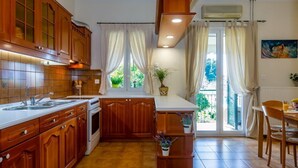 A kitchen with wooden cabinets, a built-in oven, a sink, and a window with curtains. - Casa Loula (Corfu)