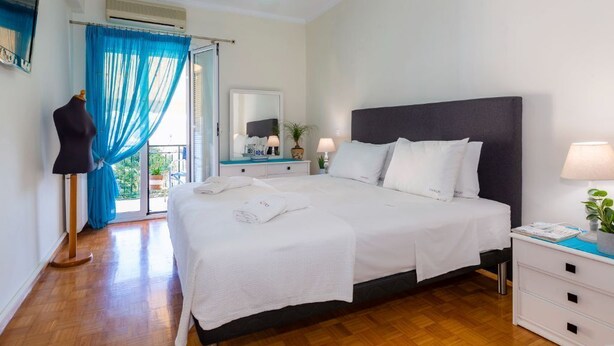 A bedroom with a large bed, a dresser, a mirror, and a window with blue curtains. - Casa Loula (Corfu)