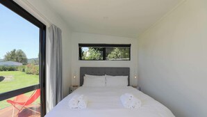 Un dormitorio moderno con una cama grande, un ventanal con vistas a la vegetación y una silla roja en el exterior.
