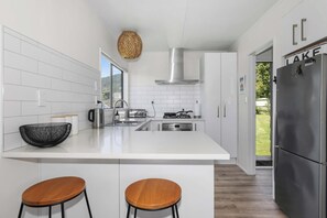 Una cucina moderna con mobili bianchi, un frigorifero in acciaio inossidabile e due sgabelli di legno.