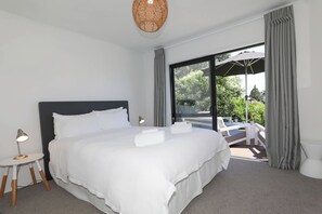 A modern hotel room with a large bed, a small side table with a lamp, and a balcony with a white chair and umbrella.