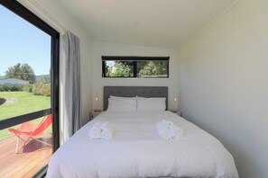 Un dormitorio moderno con una cama grande, un ventanal con vistas a la vegetación y una silla roja en el exterior.
