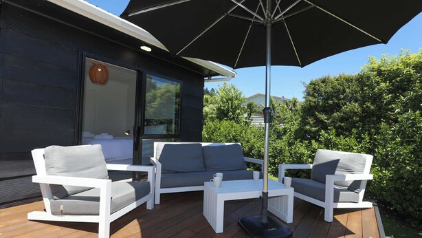 Terraza exterior con mobiliario blanco, incluyendo un sofá y sillas, bajo un parasol grande.