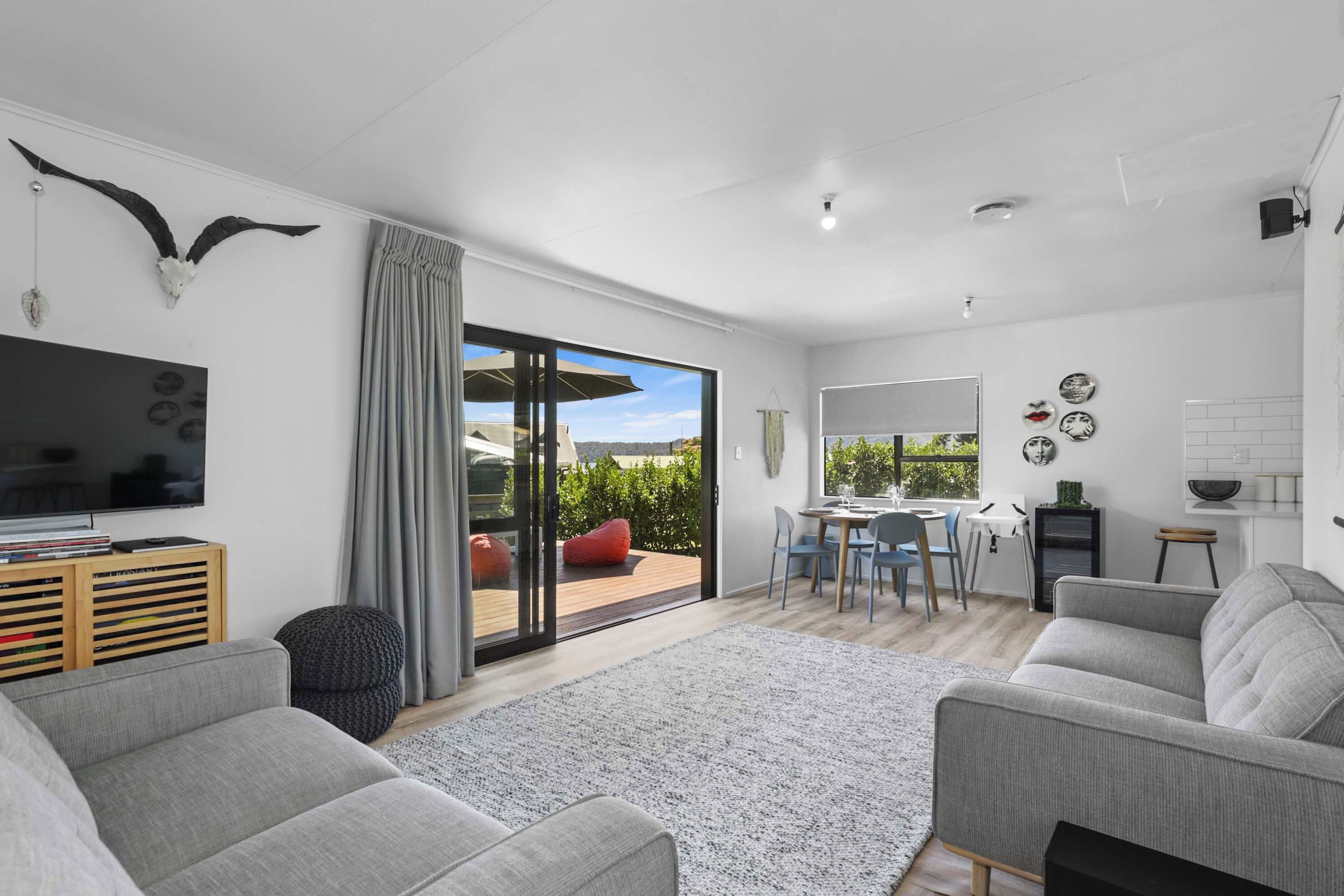 A modern living room with a grey sofa, a flat-screen TV, and a large window with a view of the outdoors.
