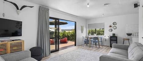 A modern living room with a grey sofa, a flat-screen TV, and a large window with a view of the outdoors.