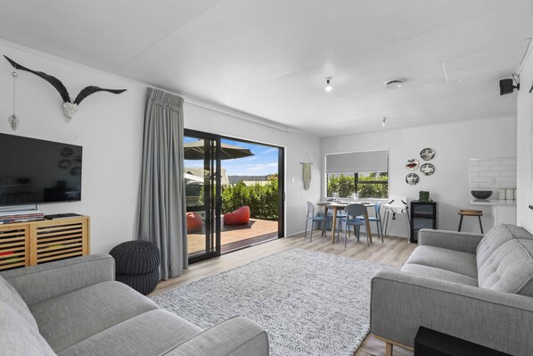 A modern living room with a grey sofa, a flat-screen TV, and a large window with a view of the outdoors.