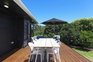 An outdoor patio with a wooden deck, a white table with chairs, and a black umbrella.