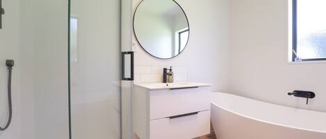 A modern bathroom with a glass shower enclosure, a white vanity with a round mirror, and a freestanding bathtub.