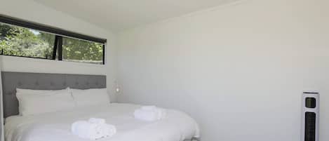 Quarto de hotel moderno com uma cama grande, aquecedor vertical e janela com vista para árvores.