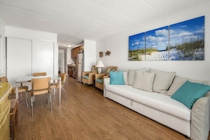 Een moderne woonkamer met een bank, stoelen, een eettafel en een keuken op de achtergrond.
