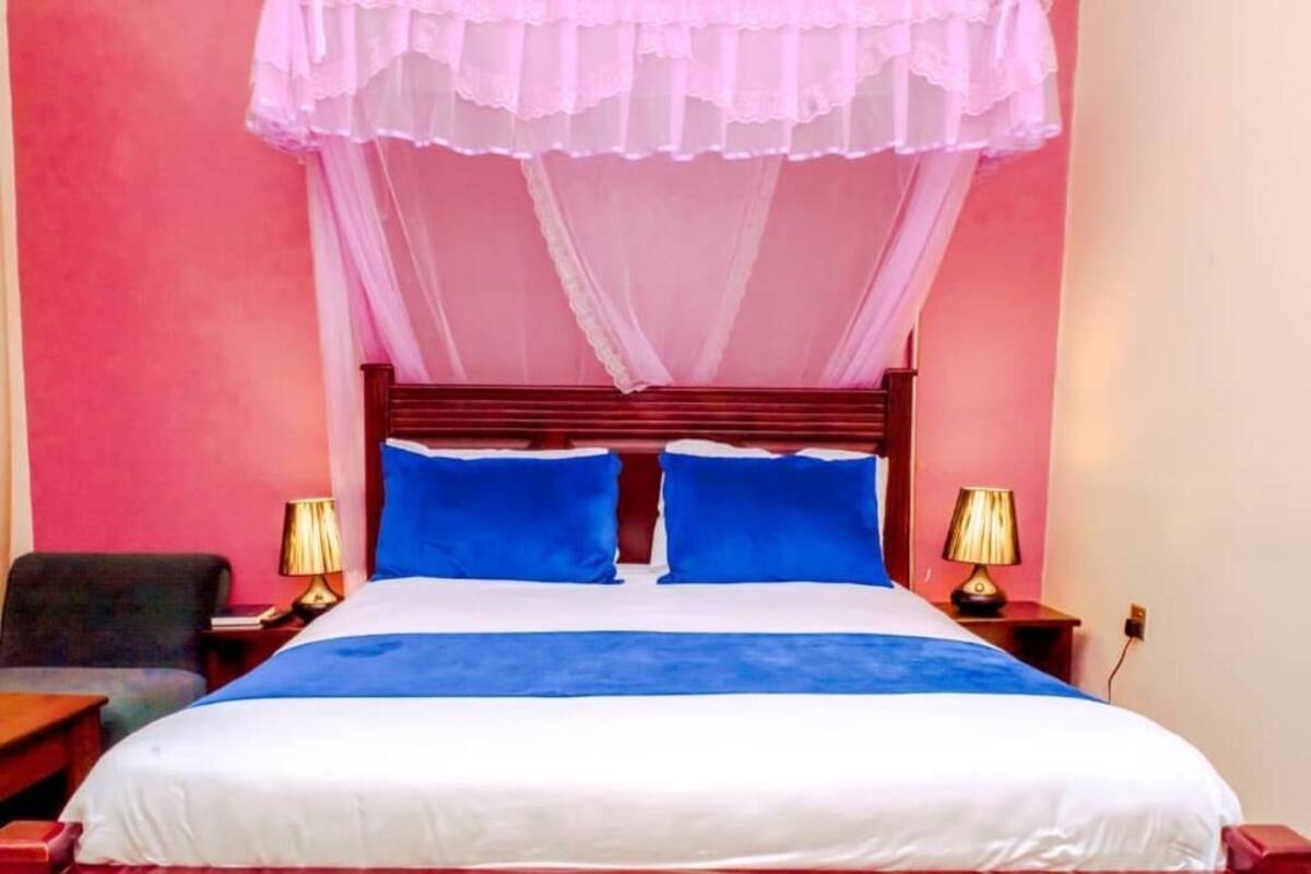 A bed with a canopy, two bedside lamps, and a chair.
