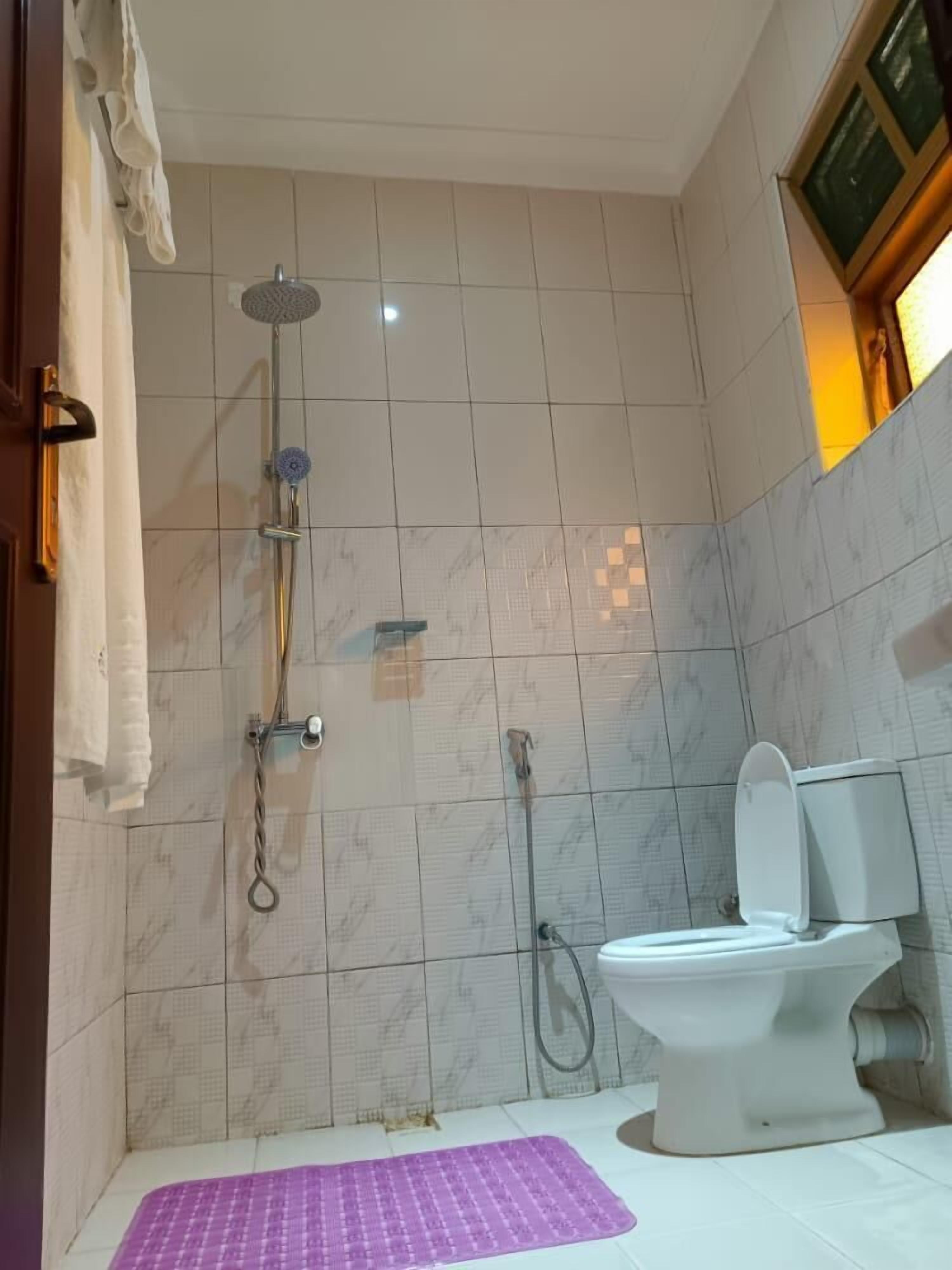 Un baño con ducha, inodoro y un tapete morado en el suelo.