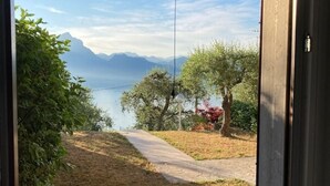 Blick aus einem Fenster auf einen Weg, der zu einem See mit Bergen im Hintergrund führt.