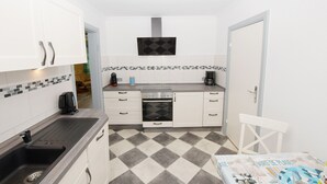 A compact kitchen with white cabinets, a black stove, and a tiled backsplash. - Ferienwohnung Hummer (Büsum)