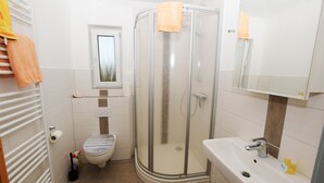 A bathroom with a glass shower enclosure, a toilet, a sink, and a mirror. - Ferienwohnung Hummer (Büsum)