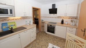 Een kleine keuken met witte kastjes, een magnetron, een fornuis en een koffiezetapparaat.