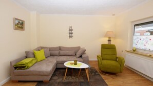 Ein Wohnzimmer mit grauem Sofa, einem grünen Sessel, einem kleinen weißen Tisch und einem gemusterten Teppich.