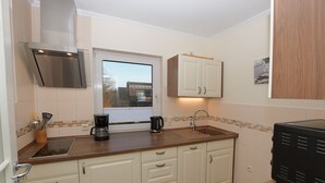 A compact kitchen with white cabinets, a stainless steel range hood, a window with a view, and a coffee maker.