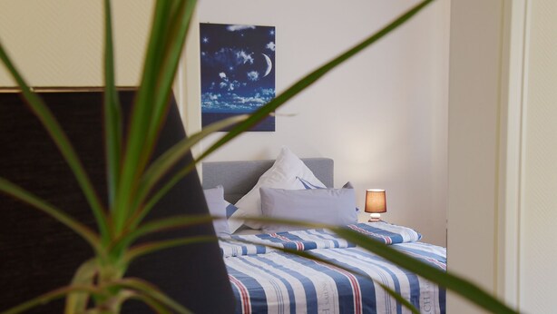 A bedroom with a bed, pillows, a nightstand, a lamp, and a wall-mounted painting.